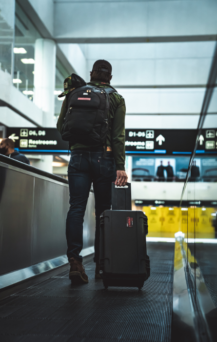 Reisender am Flughafen mit schwarzem SKB-Softcase auf Rollen und Rucksack, geeignet für den sicheren Transport von Ausrüstung auf Reisen.