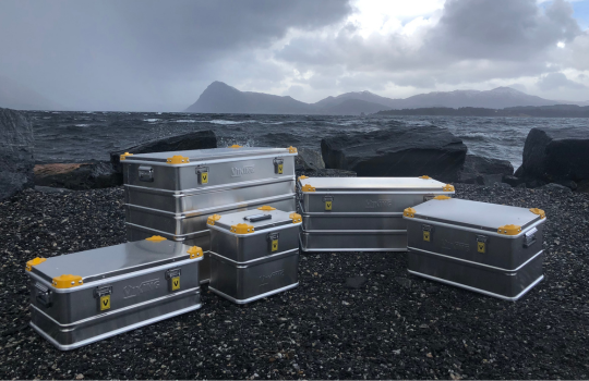 Viking Aluminium Transportkisten mit gelben Ecken auf einer felsigen Küste aufgestellt, mit Meer und Berglandschaft im Hintergrund.