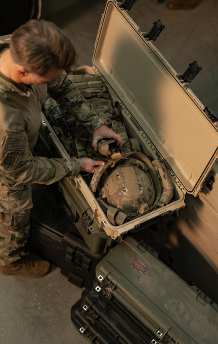 Geöffneter SKB-Hartschalenkoffer, in dem militärische Ausrüstung aufbewahrt wird, während eine Person in Militäruniform den Inhalt in einer Innenumgebung ordnet.