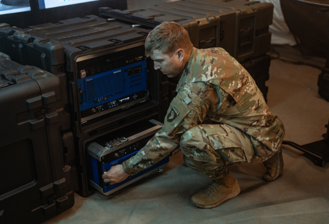 Militärangehöriger arbeitet an einem offenen 19-Zoll-SKB-Shock-Rack mit integrierter Elektronik, umgeben von mehreren geschlossenen 19-Zoll-SKB-Racks in einer Einsatzumgebung.