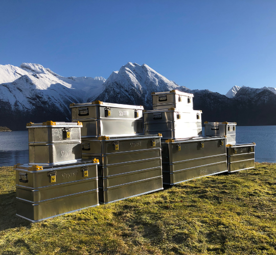 Gestapelte Aluminiumkisten von Viking in einer bergigen Landschaft an einem See
